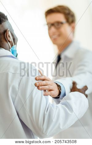 Young doctor in a lab coat congratulating colleague by patting him on shoulder