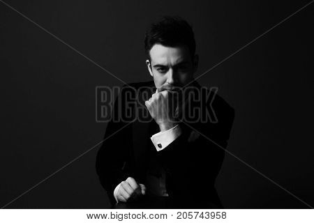 Black and white portrait of a serious young handsome man dressed in black, dramatic lighting, hand to the face, looking at the camera.