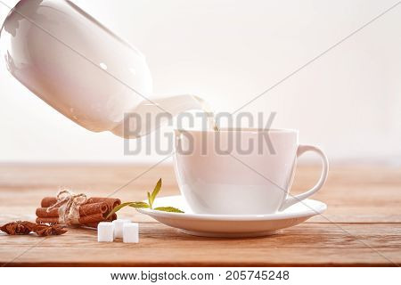 cup with green tea and teapot on light wooden table background