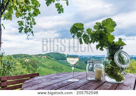 Glass white wine and jars with grapes and candle on wooden barrel near vineyard on south Styrian wine route in Austria