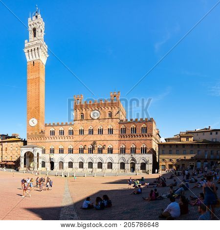 SIENA,ITALY - JULY 23,2017 : Tourists at Piazza del Campo next to the Palazzo Publico on the medieval city of Siena