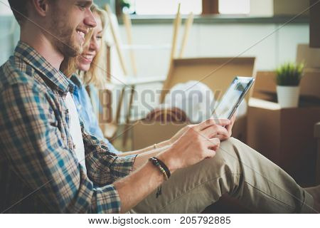 Young couple moving in new home.Sitting and relaxing after unpacking.Looking something on laptop. Young couple