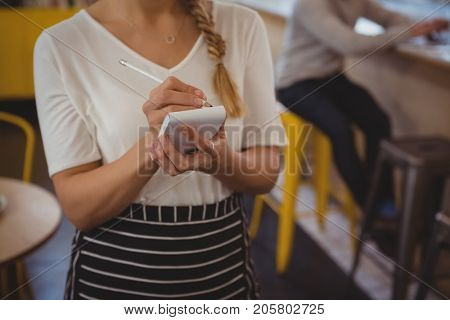 Mid section of waitress taking order by businessman at cafe