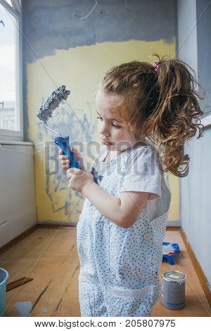 Little girl holding paint roller by hands at room