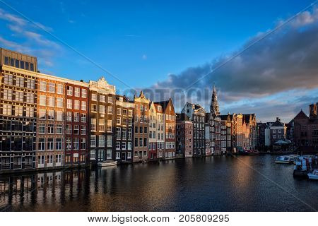 Houses and tourist boats on Amsterdam canal pier Damrak on sumset. Amsterdam, Netherlands