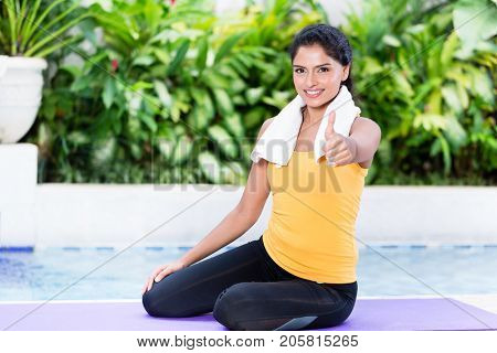 Fit young woman showing thumb up during workout routine on exercise mat outdoors