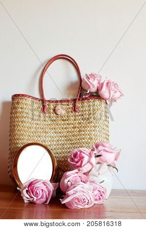Straw shabby chic bag with blush pink roses and a brass frame against a neutral painted wall. Rustic country style. Space for text