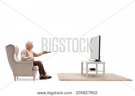 Elderly woman seated in an armchair watching television and changing channels isolated on white background