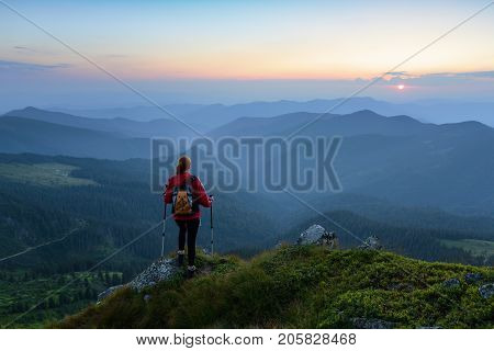 Sporty girl with back sack is standing at the edge of the precipice and watching on the endless cast of mountains landscape in the sunny day.