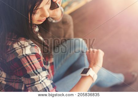 Let me check the time. Top view on a young woman wearing a wrist watch checking time while sitting on a sofa and talking with a business partner on a cellphone.
