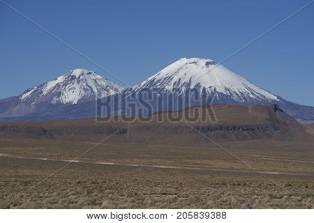 Snow covered Parinacota volcano (6342m) towering above the Altiplano and cliffs running along the valley of the River Lauca in Lauca National Park, northern Chile.