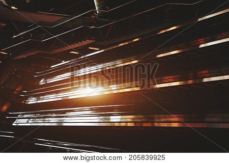Wide-angle shooting of moving staircase in dark hall of modern airport terminal; interior of mall or railway station with empty escalators following opposite sides strong flare from sun reflection