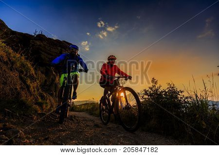 Cycling women and man riding on bikes at sunset mountains forest landscape. Couple cycling MTB enduro flow trail track. Outdoor sport activity.