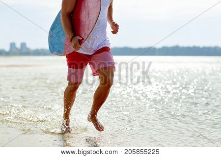 skimboarding, water sport and people concept - happy smiling young man with skimboard on summer beach