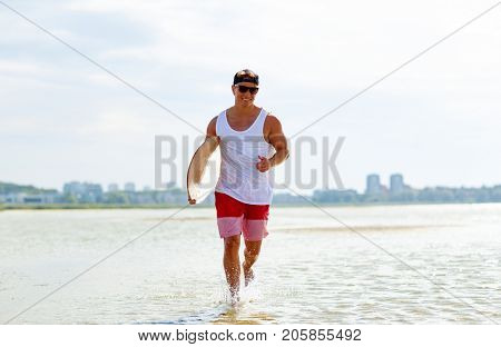 skimboarding, water sport and people concept - happy smiling young man with skimboard on summer beach