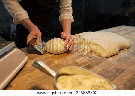 food cooking, baking and people concept - chef or baker making bread and portioning dough with bench cutter at bakery