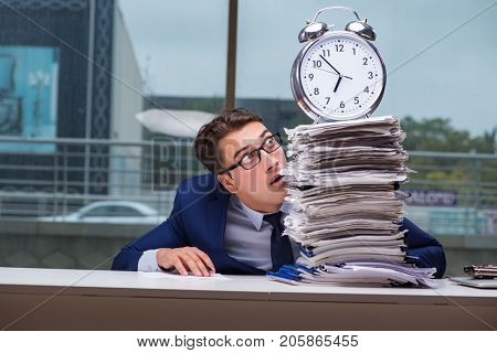 Businessman with pile stack of paper paperwork and an alarm cloc
