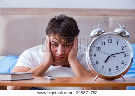 Man in bed frustrated suffering from insomnia with an alarm cloc