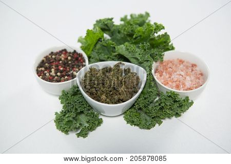 High angle view of salt and peppercorns with kale on white background