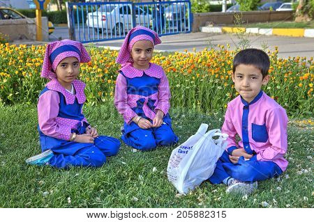 Fars Province Shiraz Iran - 19 april 2017: Three preschool children two girls and one boy dressed in lilac uniform sit on the lawn grass in the city park.