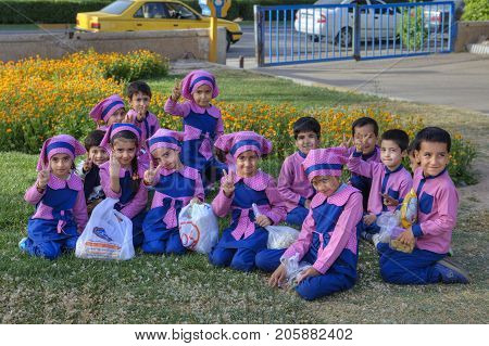Fars Province Shiraz Iran - 19 april 2017: A group of children boys and girls of pre-school age dressed in pink and blue uniforms posing for photographer sitting on the lawn grass in city park.