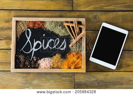 Various type of spices on slate and digital tablet on wooden table