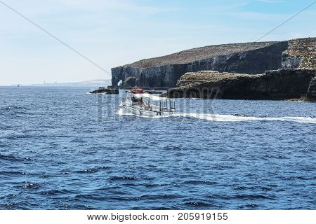 Comino is a small island of the Maltese archipelago between the islands of Malta and Gozo in the Mediterranean Sea. Pleasure craft at the rugged coastline delineated by sheer limestone cliffs and dotted with deep caves