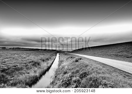 Agriculture on Land Reclaimed from the See in Netherlands. Asphalt road along protective dam and canal in Holland. Black and white picture
