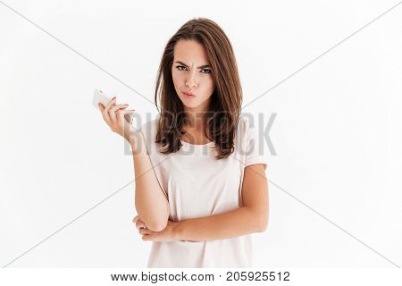 Serious brunette woman with smartphone in hand looking at the camera over white background