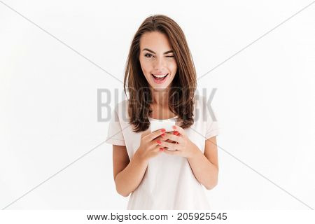 Happy brunette woman holding smartphone and winks at the camera over white background