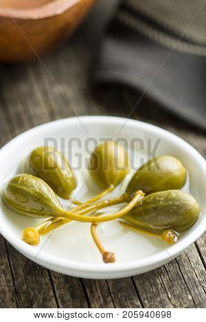 Pickled caper berries in bowl on old wooden table.