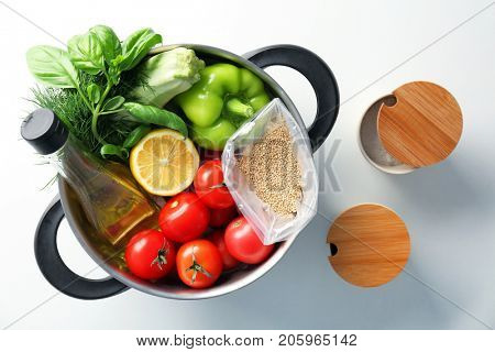 Composition with uncooked quinoa and products in stewpan on white background