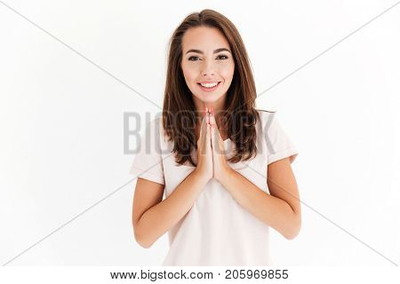 Smiling brunette woman holding hands in pray gesture and looking at the camera over white background
