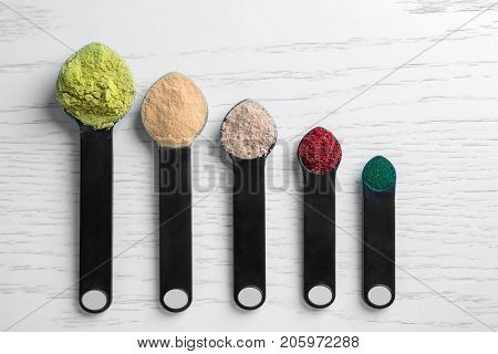 Composition with various colorful superfood powders and measuring spoons on wooden background