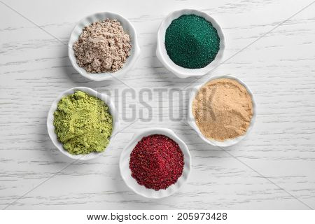Various colorful superfood powders in white ceramic bowls on wooden background