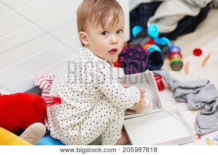 Cute Baby Girl In Pajamas Squatting On Floor Tries To Put On Her White Shoes