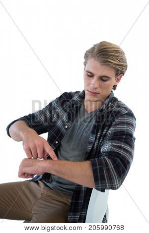 Young businessman pointing on imaginary wristwatch while sitting on chair against white background