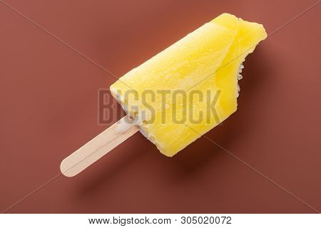 Yellow Popsicle With Bites On A Brown Background