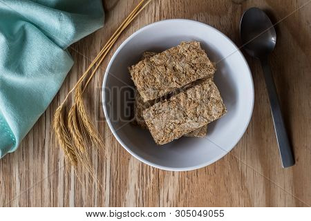 Wheat Cereal In Bowl With Wheat Spears On Wooden Table With Spoon And Napkin - Top View Photo