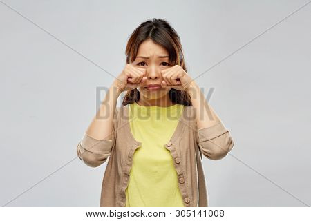 people, emotion and gesture concept - sad asian woman crying over grey background