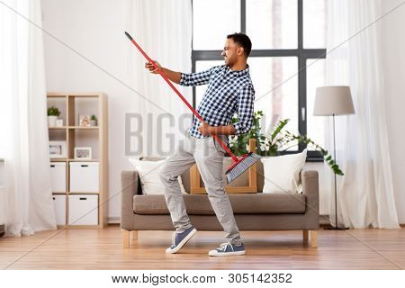 cleaning, housework and housekeeping concept - indian man with broom sweeping floor and having fun at home