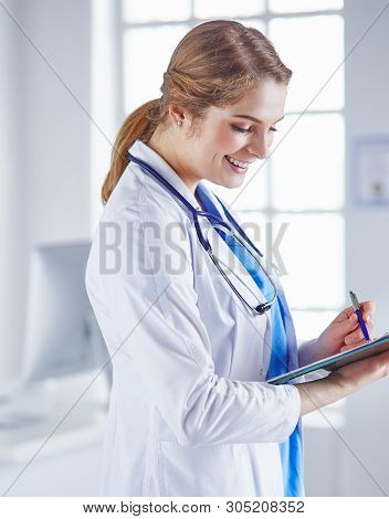 Young Woman Doctor Is Standing With Board With Clipboard Smilin