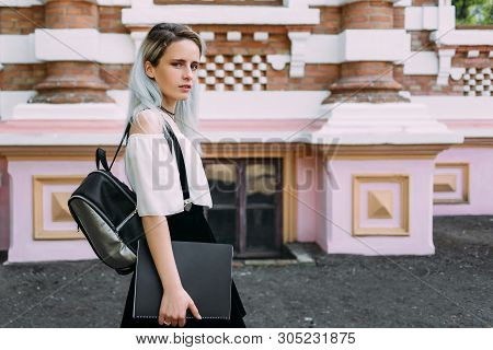 Pretty Student Stands With A Black Folder And A Backpack Against The Background Of The Architektura.