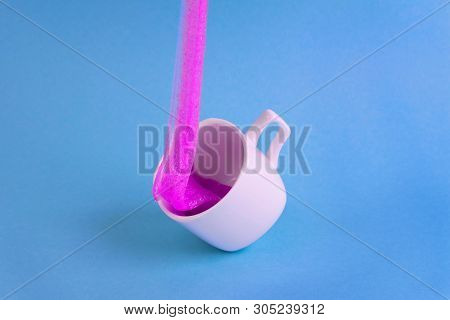 Bright Pink Glitter Slime Comes In Mug. White Cup On Blue Background. Art Neon Surrealism And Minima