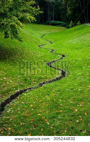 Winding Drain Outfall On Fresh Green Trimmed Lawn With Fallen Yellow Leaves. Winding Ditch On Green 