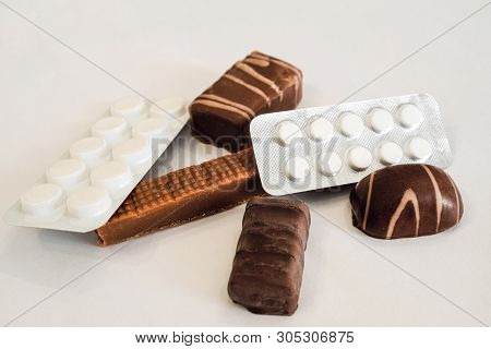 Chocolate Candies And Pills Lie On A White Table. Concept Of Dangerous Neighborhood Medicaments And 