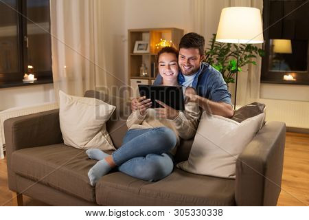 technology, internet and people concept - happy couple using tablet computer at home in evening