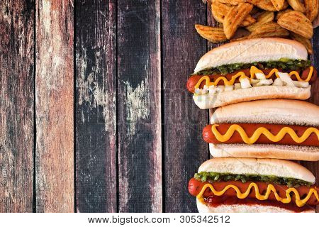 Hot Dogs With Toppings And Potato Wedges. Side Border, Top View On A Dark Wood Background With Copy 