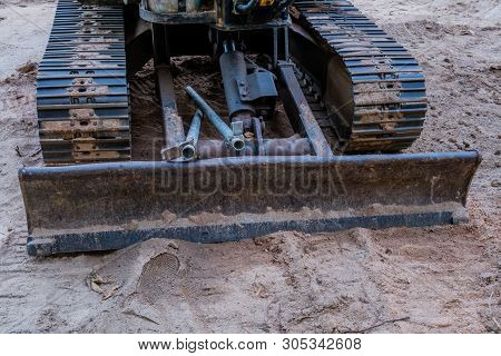 Front View Of Back Hoe Tracks And Attached Dirt Moving Blade At Construction Site.