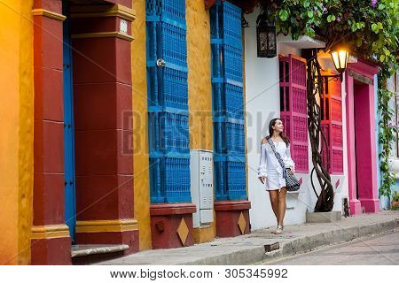 Beautiful Woman On White Dress Walking Alone At The Colorful Streets Of The Colonial Walled City Of